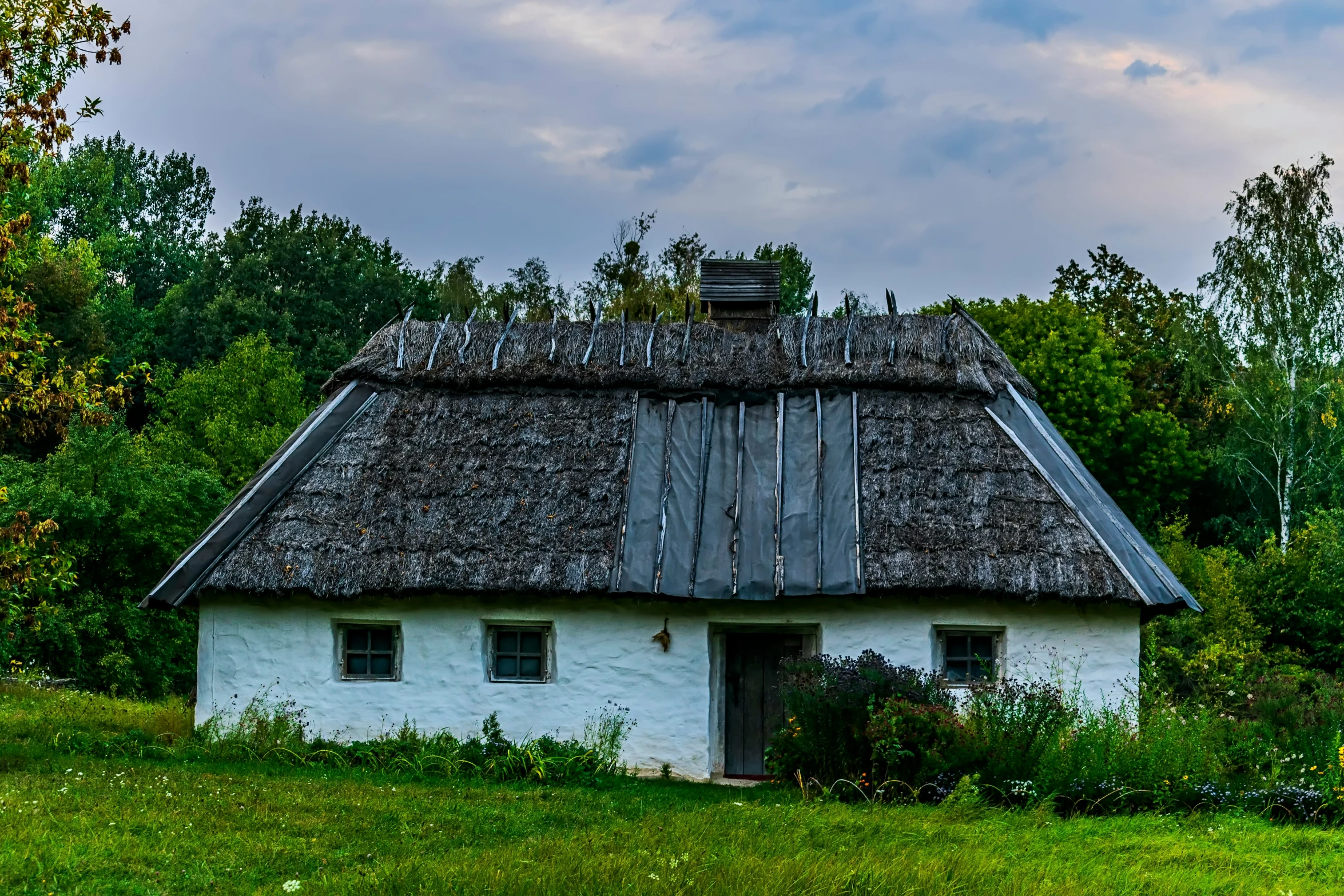 old white building in middle of green field with trees and clouds