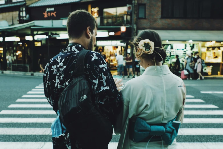 a man and a woman stand on the street waiting to cross