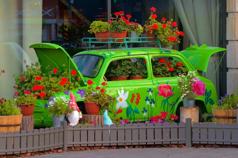 a green toy car with some red flowers behind it