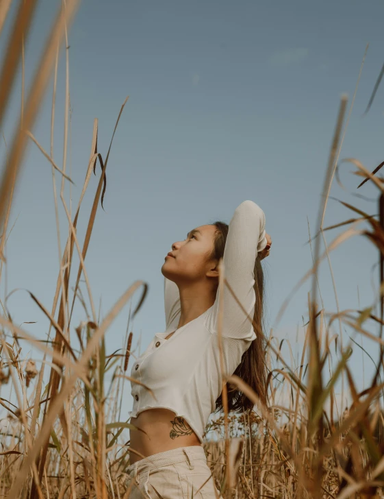 a woman standing in tall dry grass under a blue sky