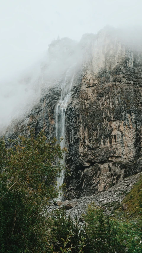 a mountain side with a large waterfall covered by fog