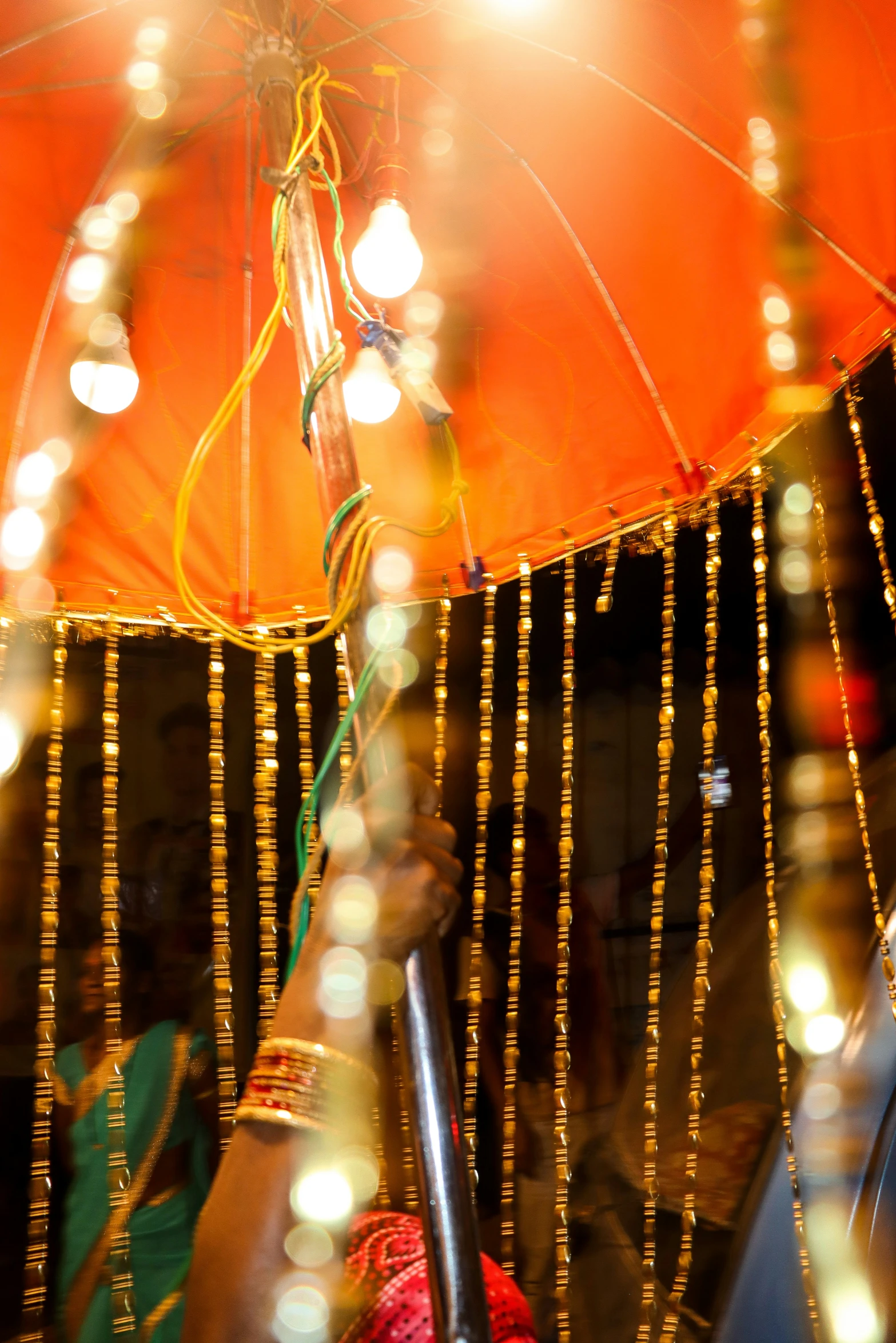 a person holding an orange umbrella with gold strings on them