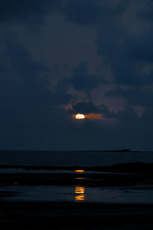 a beach at night with the moon lit up over the water