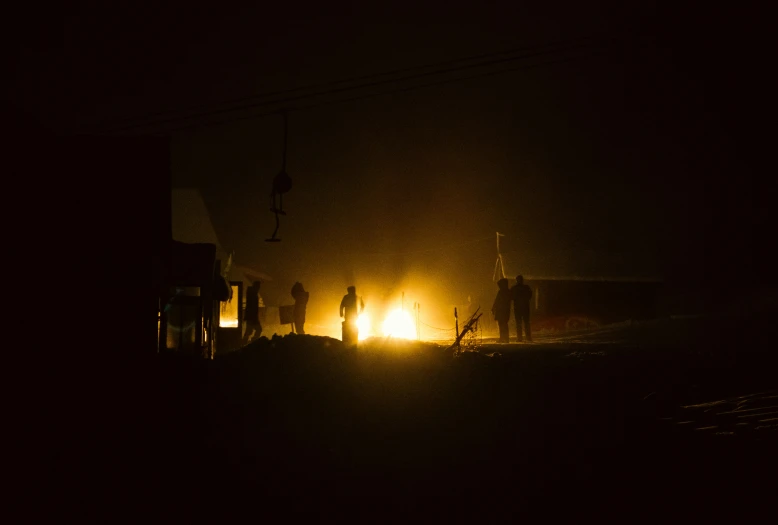 two men are standing outside at night with a bright yellow flame