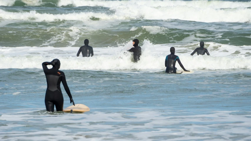 people in wet suits with surfboards in water