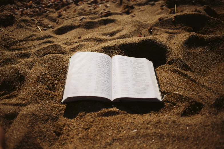 a book with white pages lies on a sandy beach