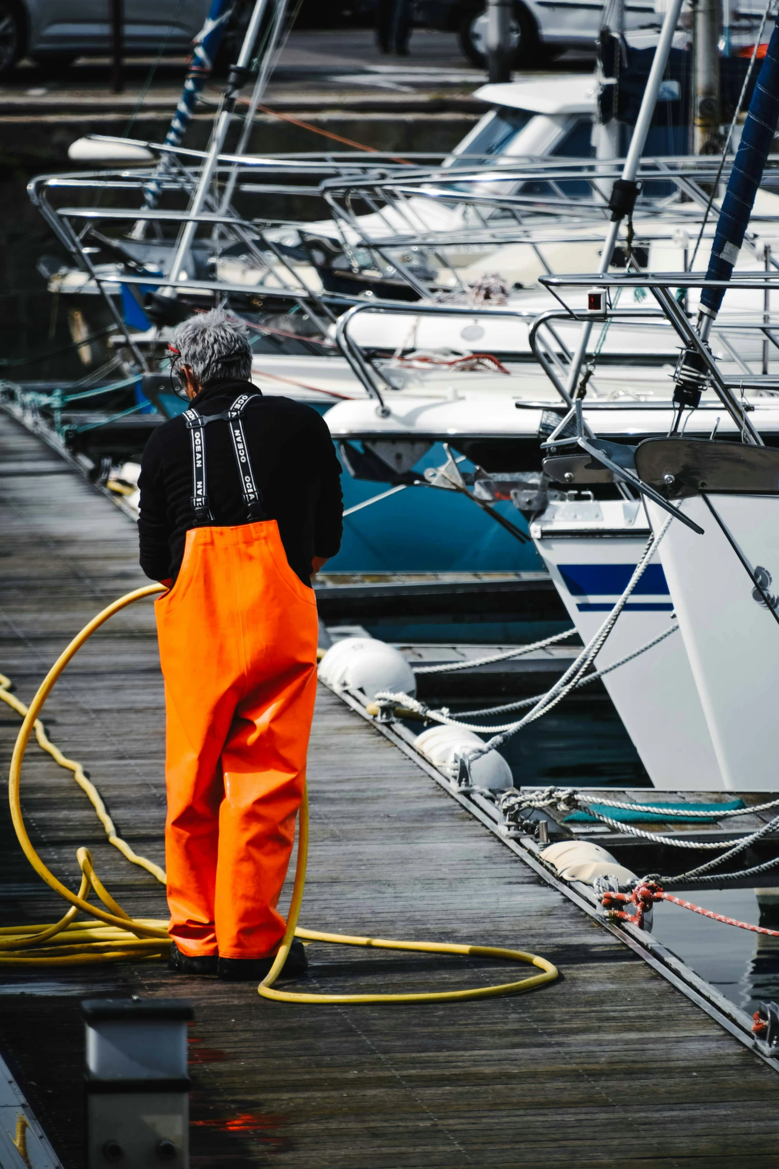 man in orange overalls standing on pier with ropes and hose