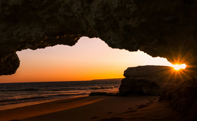 sun setting from inside of a cave with waves crashing