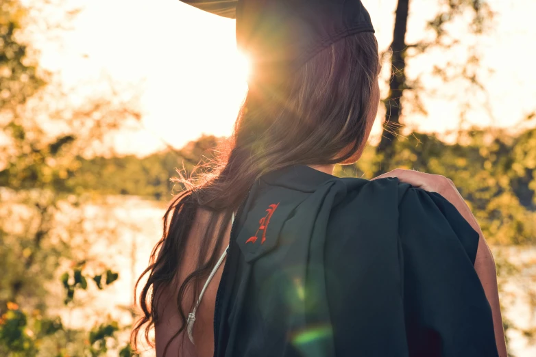 woman in cap and gown standing near water at sunset