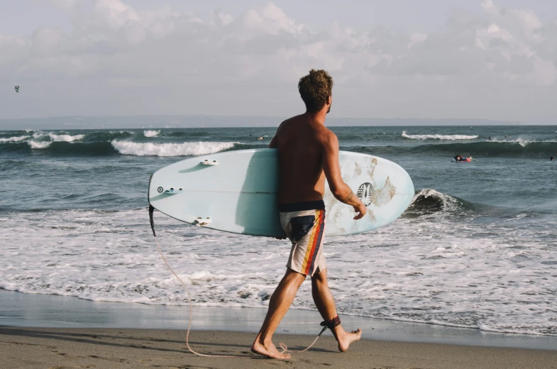 a man walks down the beach holding a surf board