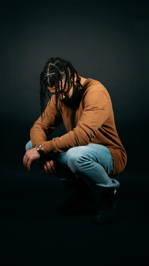 the man with dreadlocks is sitting in a black backdrop