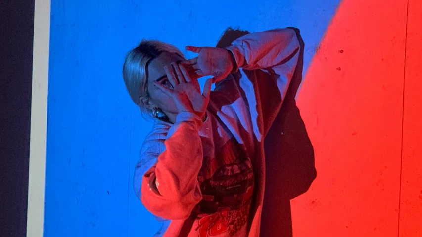 a young woman leans on a wall with red and blue walls