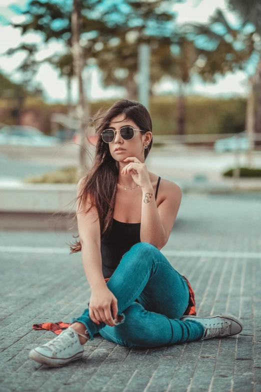 a woman in sunglasses is sitting on the ground and is looking into the distance