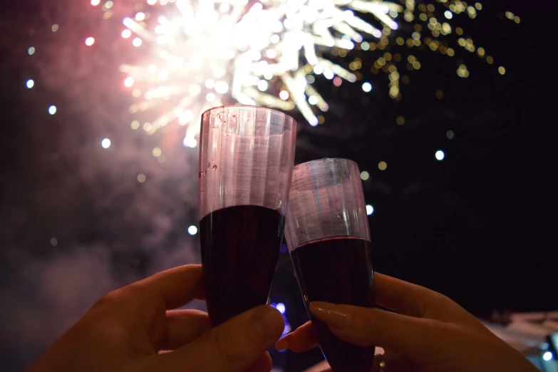 a pair of people that are holding champagne in front of a fireworks