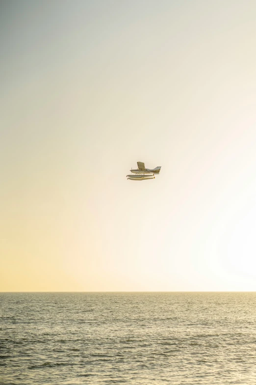 a plane is flying over the ocean at sunset