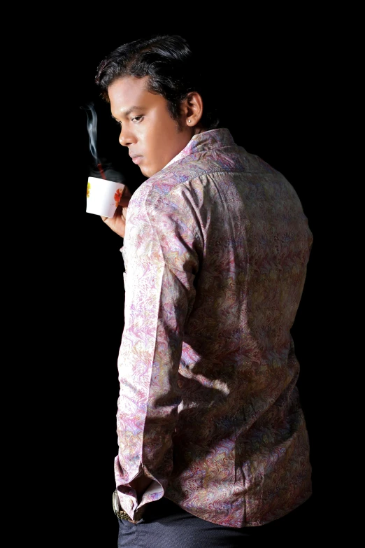 a man holding a mug standing against a black background