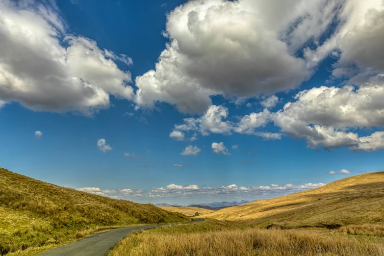 two roads winding uphill with blue skies and clouds above