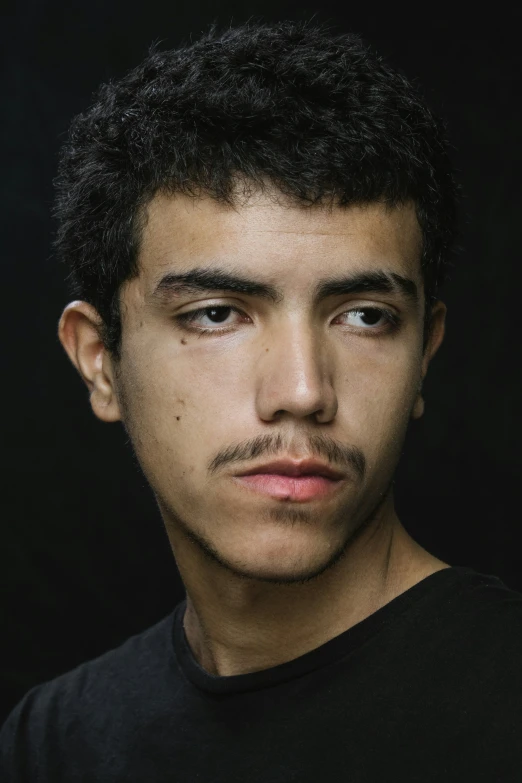 a man with a moustache looks forward in a black shirt