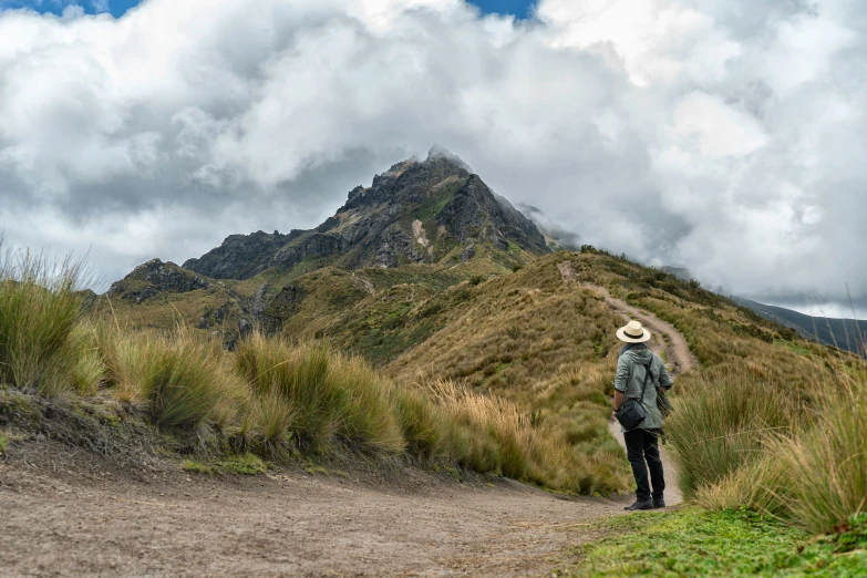 a man with a straw hat standing on a mountain trail