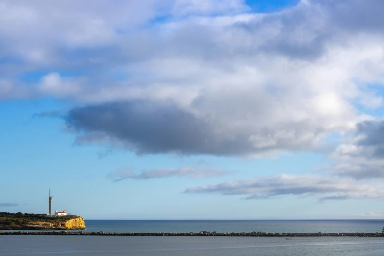 a lighthouse stands atop the shoreline as clouds loom over the water