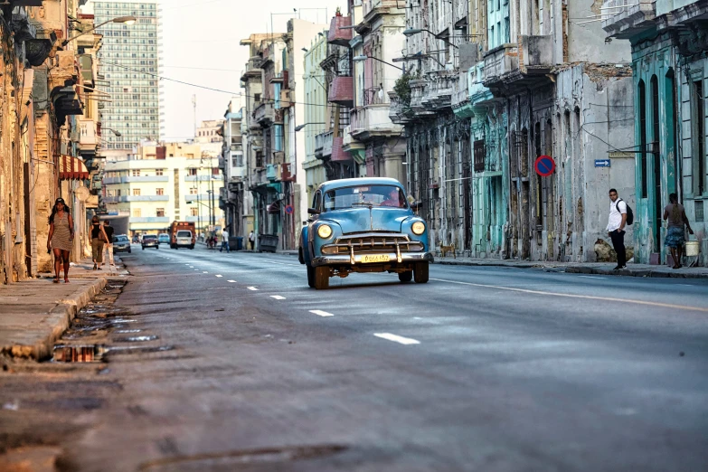 an old blue car driving down the street