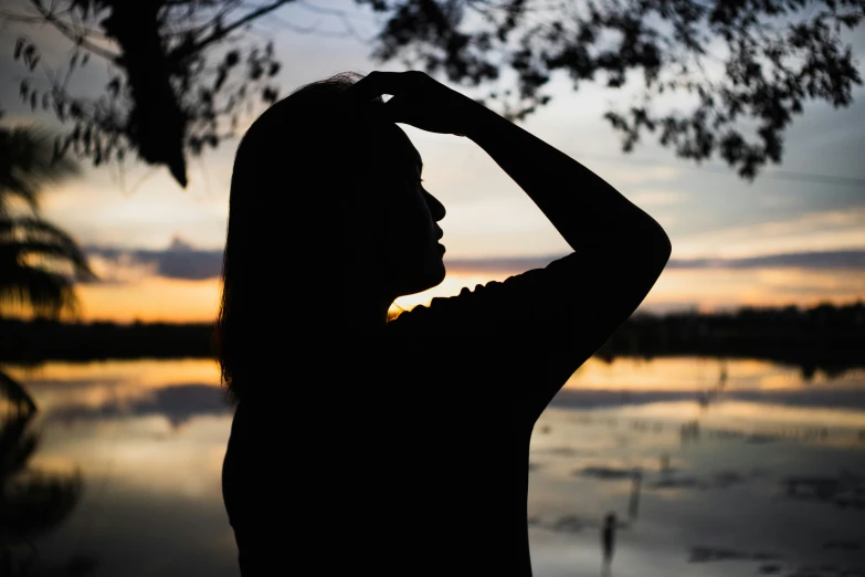 silhouetted woman in front of sunset overlooking lake