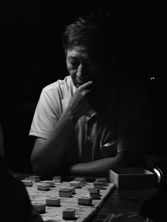 man sitting at a table looking down at a board game