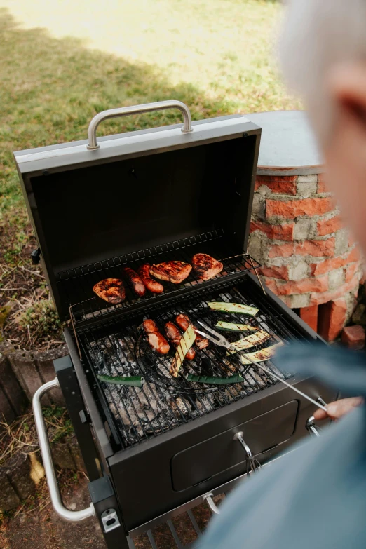 a man holding a silver tray with chicken and vegetables cooking on it