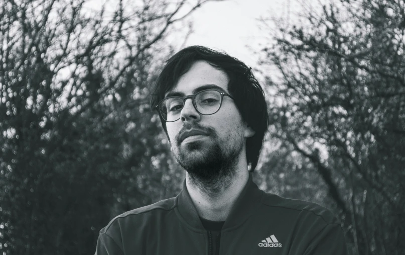 a bearded man standing in front of trees