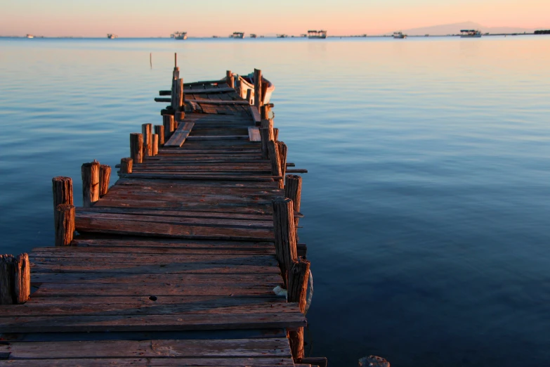 an old dock sits in a calm water at sunrise