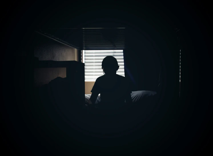 a dark room with someone sitting by the bed