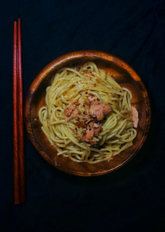 the bowl on the table holds noodles, meat and chopsticks