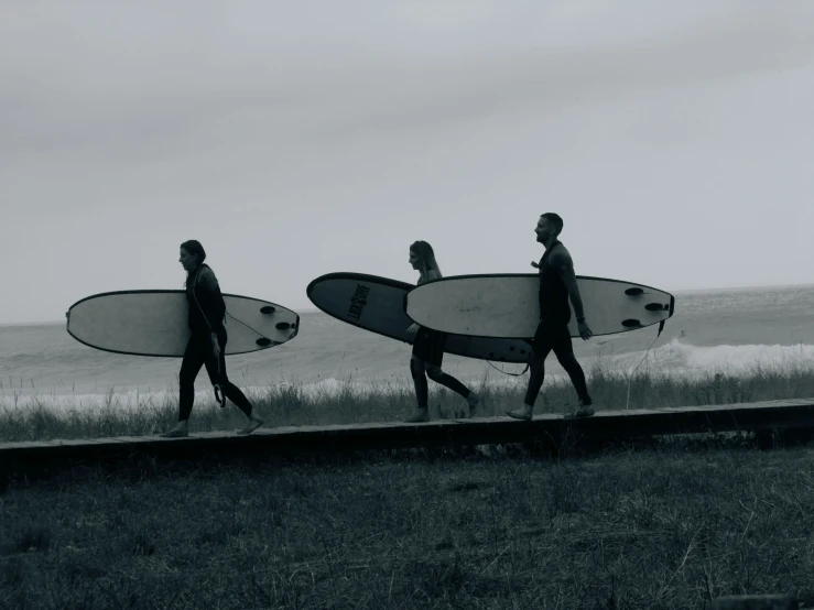 three people holding surfboards walking across the grass