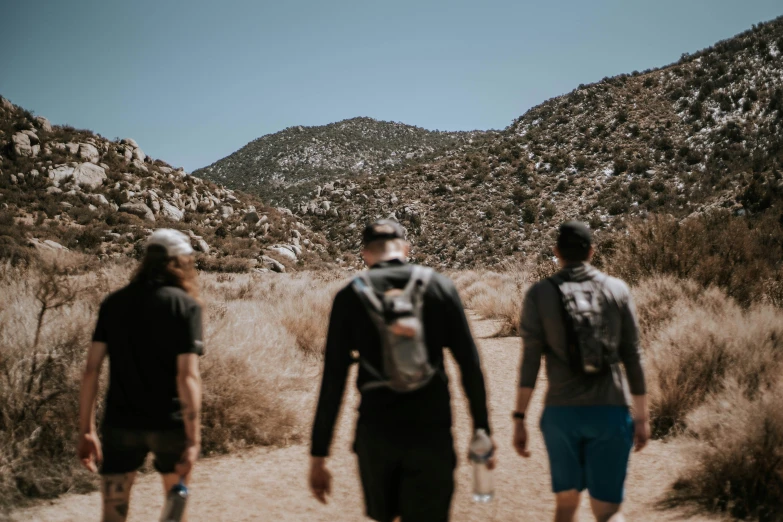 two men walking down a dirt road with a hill in the background