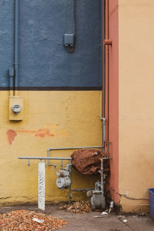 a pipe next to a yellow and blue wall with some rust