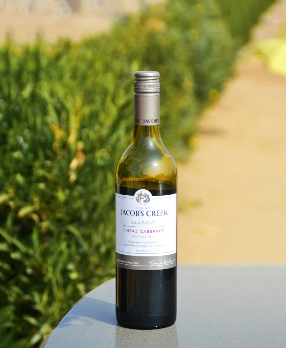 a bottle of wine sitting on top of a table next to a bush