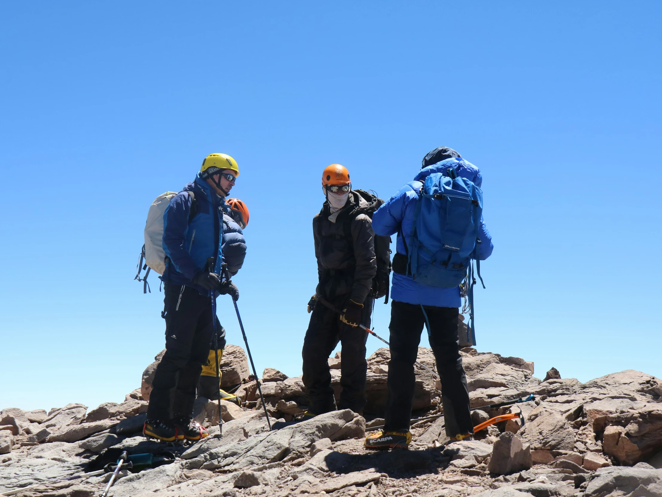 three men standing on a mountain wearing gear