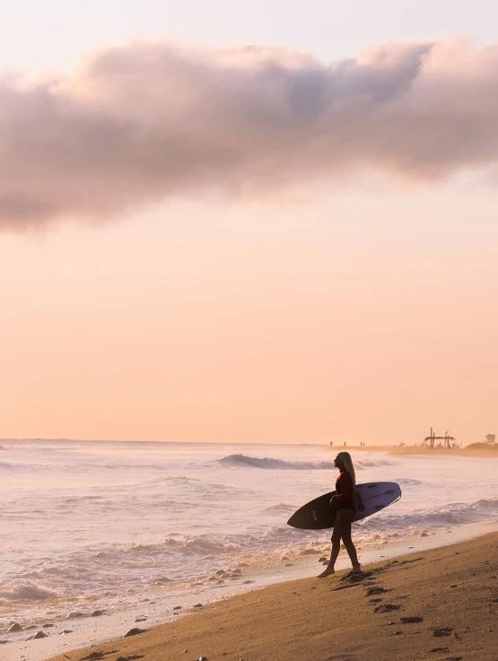 a woman walking on the beach holding her surfboard