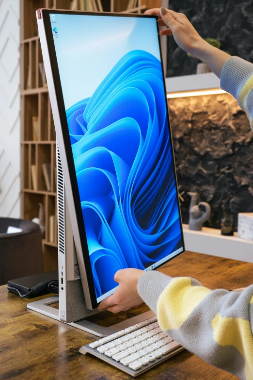 a man holding the screen of a computer on his desk