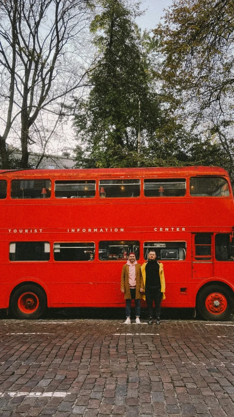 two people stand in front of a large double decker bus