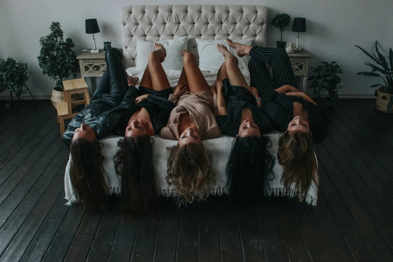 five woman lie on the bed and are looking at the camera