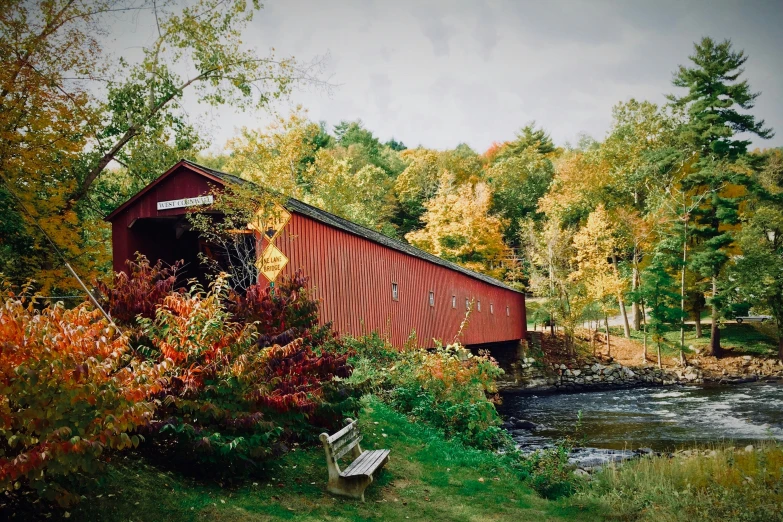 a covered train bridge crosses over a small river in the woods