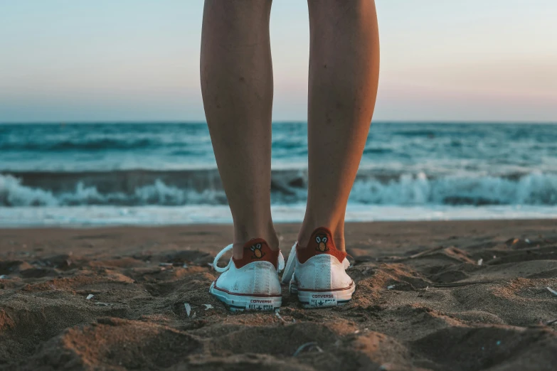 person's legs in sneakers standing on beach