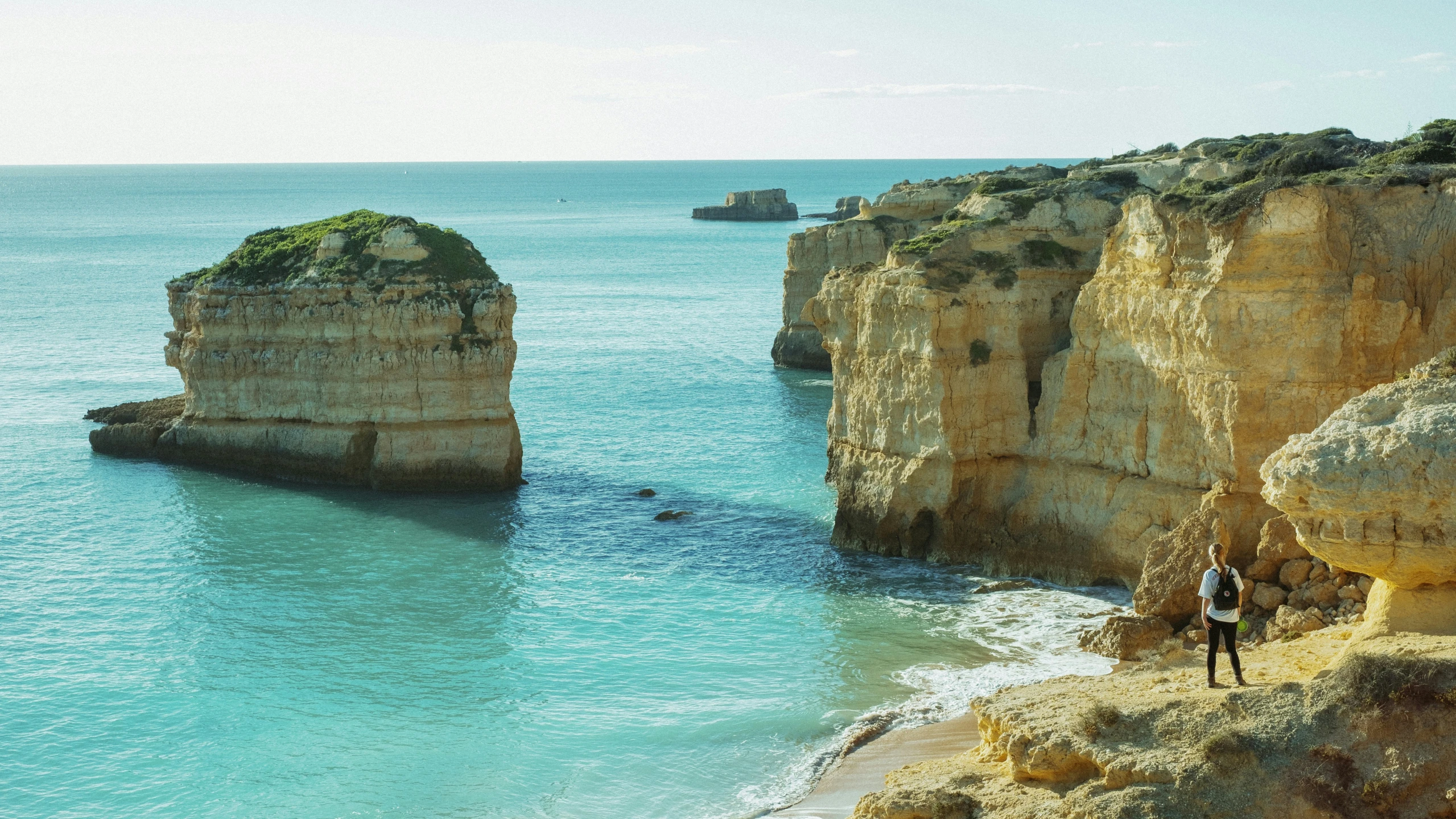 a man walking in a canyon on the edge of a cliff near an ocean with a couple people on it