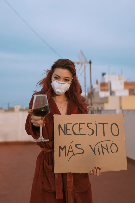 a woman in a mask holds a sign with a glass of wine