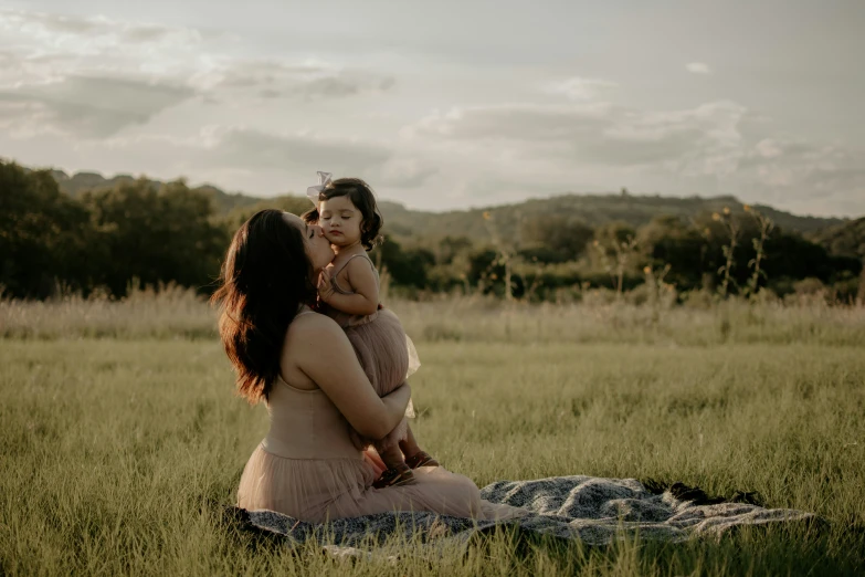 a pregnant woman holds her daughter in her arms while she sits down in a field