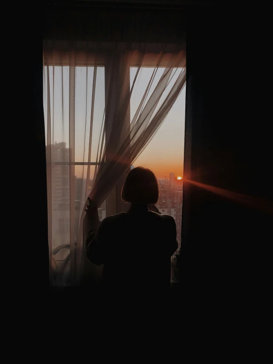 a person looking out of a window at the sun setting