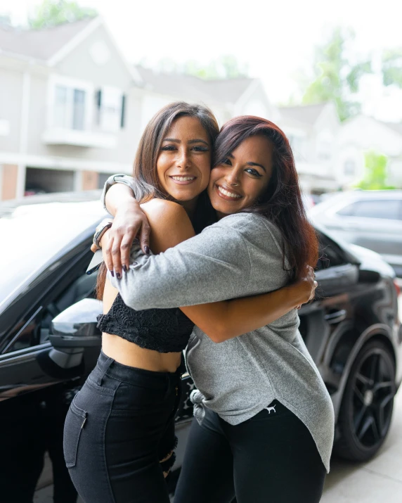 two women hugging each other while standing near a car