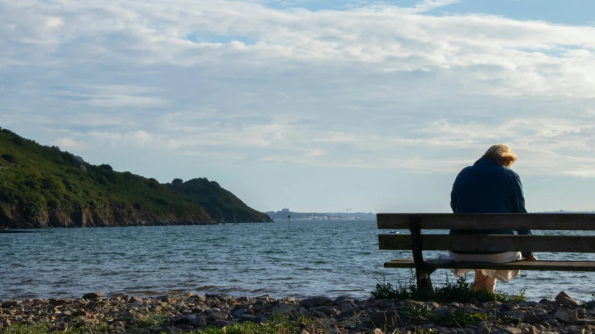 the man sits on a bench in front of the water