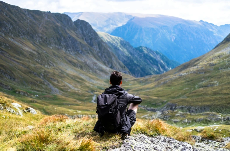 a man sits on top of a hill looking down at the valley below